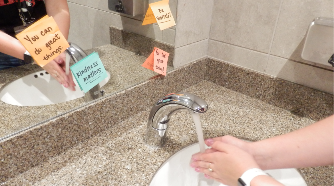 Student washes their hands while reading the encouraging messages posted by Rachel's Challenge.